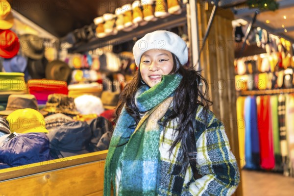 Young woman wearing a beret and scarf, smiling at a christmas market stall selling winter clothes and accessories