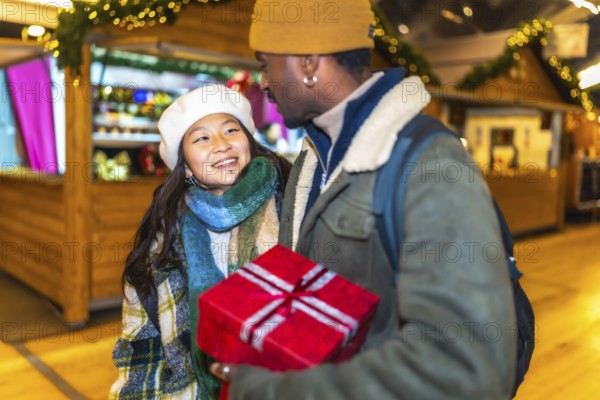 Young multiethnic couple holding a christmas gift, enjoying christmastime at a christmas market