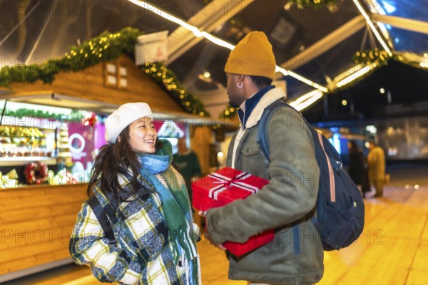 Young multiethnic couple exchanging christmas gifts at a christmas market, enjoying the festive atmosphere and holiday spirit