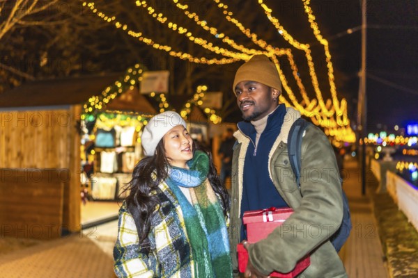 Young multiethnic couple walking and enjoying christmastime at a decorated outdoor market with festive lights