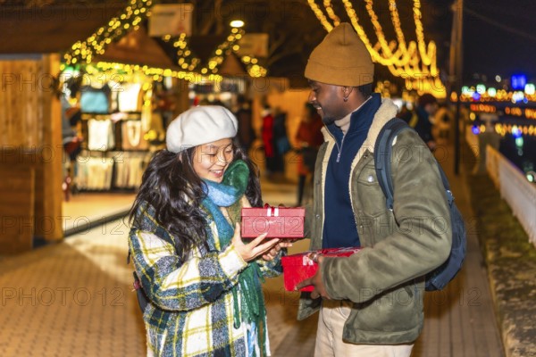Happy multiethnic couple exchanging christmas gifts at a festively decorated christmas market, enjoying the magical atmosphere and celebrating together