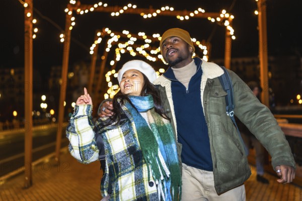 Young multiethnic couple walking hand in hand, admiring the enchanting christmas lights and festive decorations on a winter night