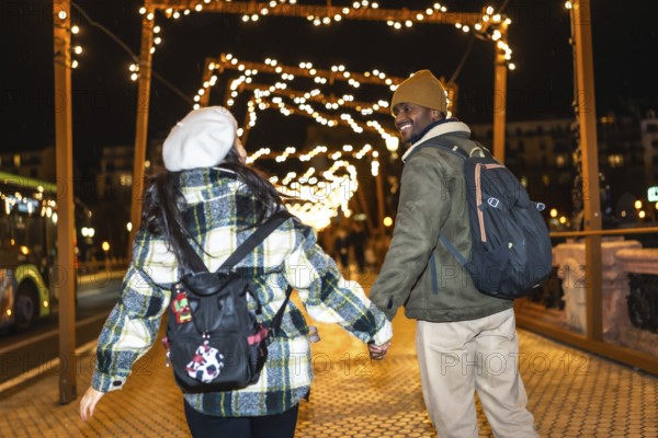 Multiethnic couple walking hand in hand under glowing christmas lights, enjoying a magical night filled with festive joy and romance