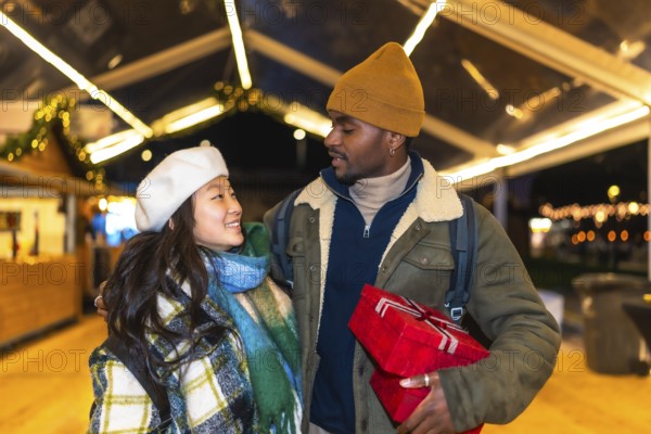 Young multiethnic couple exchanging christmas gifts and enjoying christmas time at a christmas market