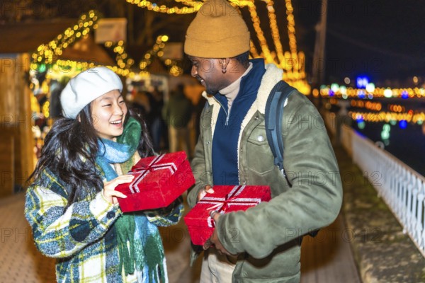 Young multiethnic couple exchanging christmas gifts at a christmas market, enjoying the festive atmosphere