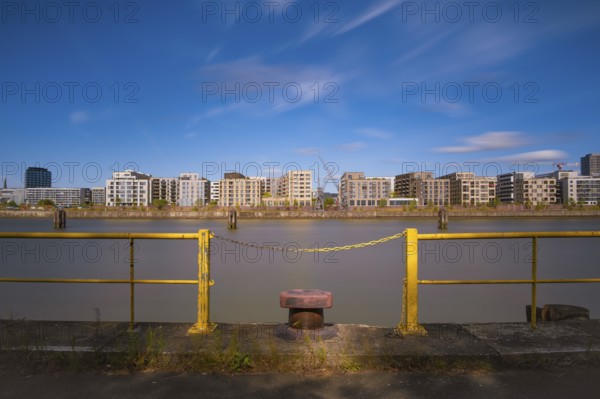 View over a harbour basin to a part of the Hamburg Hafencity in the foreground a yellow railing with a chain and a bollard, Hamburg Germany