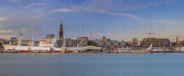 View over the Norderelbe to the main church St. Michaelis and the Landungsbrücken with ships in front of it in the evening light, long exposure, Hamburg, Germany