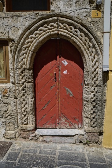 Red door with Romanesque arch and decorative stone carvings in an old façade, Turkish Quarter, Rhodes Old Town, Rhodes Town, Rhodes, Dodecanese, Greek Islands, Greece