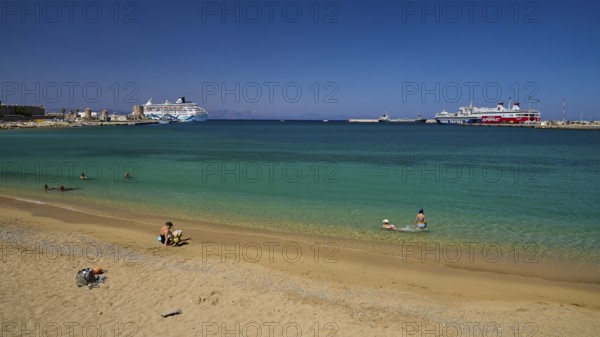 Clear water and beaches with a view of the harbour and several ships on a sunny day, Sachtouri beach, Rhodes Old Town, Rhodes Town, Rhodes, Dodecanese, Greek Islands, Greece