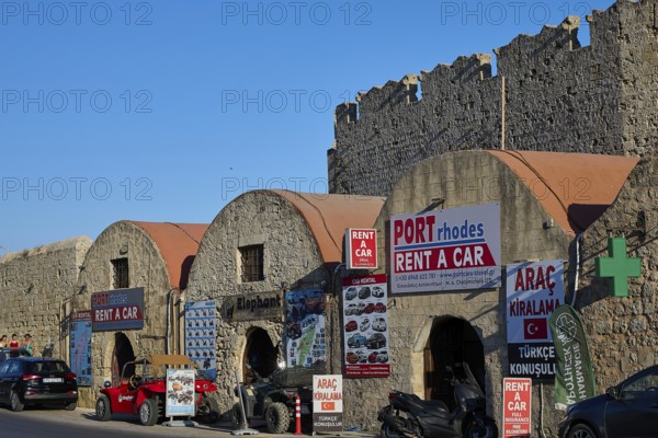 Outside the fortress walls, warehouses, row of buildings with car hire signs under historic stone arches along a city wall, Rhodes Old Town, Rhodes Town, Rhodes, Dodecanese, Greek Islands, Greece