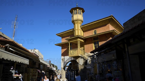 Ottoman building, Sokratous building, Lively market with people and a striking historical building with tower under a clear sky, Rhodes Old Town, Rhodes Town, Rhodes, Dodecanese, Greek Islands, Greece