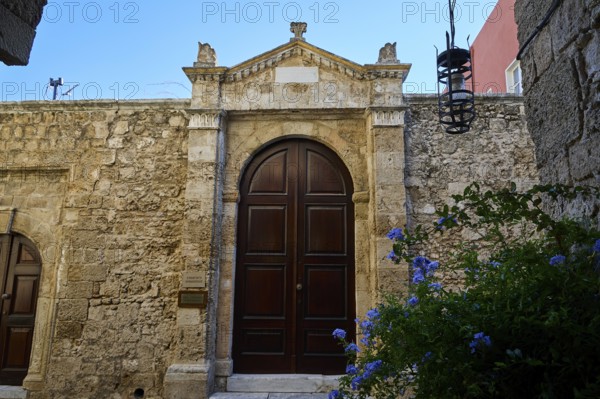 Gate of a synagogue, Massive wooden door in an old stone wall under a blue sky with blooming flowers in the foreground, Rhodes Old Town, Rhodes Town, Rhodes, Dodecanese, Greek Islands, Greece
