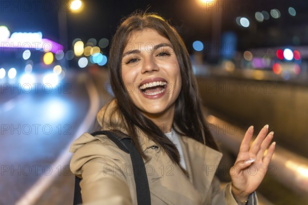 Young woman smiling and taking a nighttime selfie on a vibrant city street, capturing candid joy against glowing bokeh lights for social sharing and travel memories