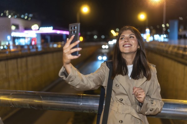 Young woman smiling and holding a smartphone, capturing a selfie against the bright, blurred lights of a busy urban street at night, enjoying personal connection
