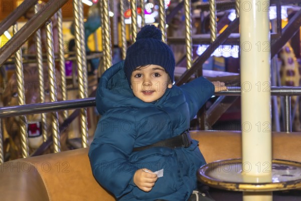 Young child wearing a blue winter coat and hat enjoying a carousel ride at a christmas market in bayonne, france