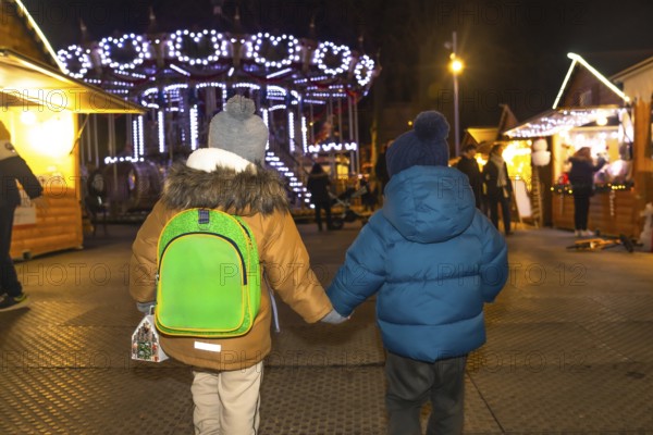Two young boys holding hands are walking through a christmas market at night in bayonne, france, enjoying the festive atmosphere
