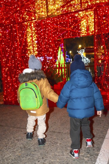 Two young boys holding hands walking through a christmas light display in bayonne, france at night