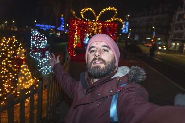 Bearded tourist taking a selfie with christmas lights and decorations in bayonne, france, at night
