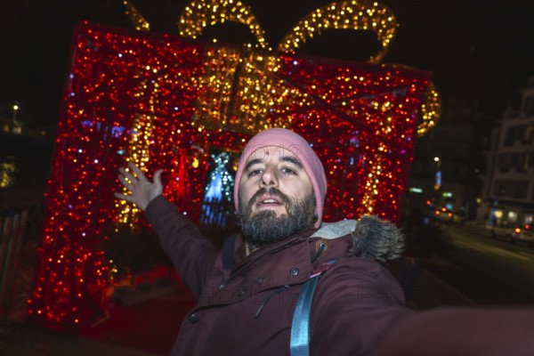 Bearded man taking a selfie in front of giant luminous christmas gift box in bayonne, france