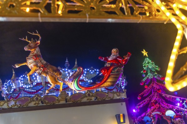 Santa claus figurine waving on a sleigh pulled by a reindeer at the bayonne christmas market in france, with christmas lights and decorations