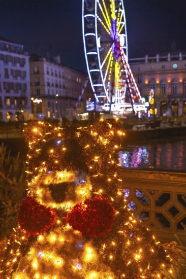 Luminous christmas bear decoration shining brightly in bayonne, france, with a ferris wheel and festive lights illuminating the background at night