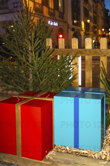 Large red and blue christmas presents sit on a wooden platform, adorned with fir branches, creating a festive atmosphere in bayonne, france
