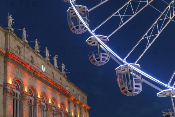 Ferris wheel cabins rotating over bayonne city hall illuminated in orange during christmas night in france