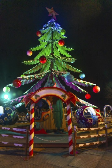 Children enjoying a carousel ride beneath a brightly lit christmas tree at a festive night market in bayonne, france