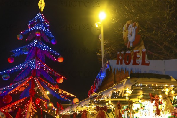 Glowing christmas tree and decorated market stall create festive atmosphere at night in bayonne, france