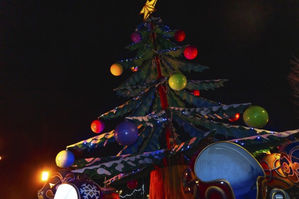Colorful christmas tree with lights and decorations illuminating a carousel at night in bayonne, france, creating a festive atmosphere