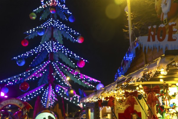Luminous christmas tree towering over festive stalls adorned with lights and decorations at the bayonne christmas market in france