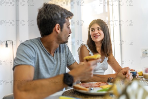 Young couple sharing a meal and conversation at their kitchen table, enjoying a relaxing morning together