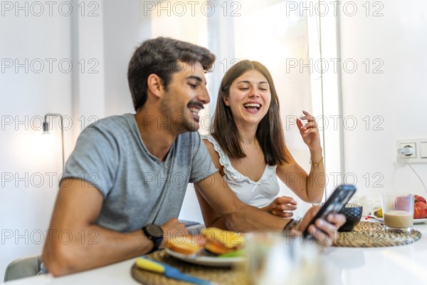 Young couple enjoying breakfast and having fun while using a smartphone in their modern kitchen