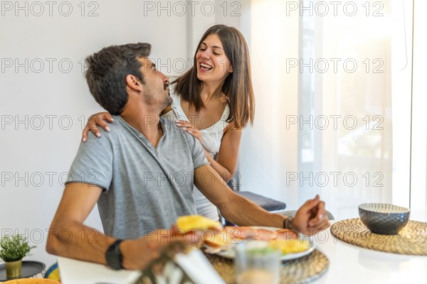 Young couple sharing a laugh during breakfast at home, enjoying a meal and each other's company in their bright, modern kitchen
