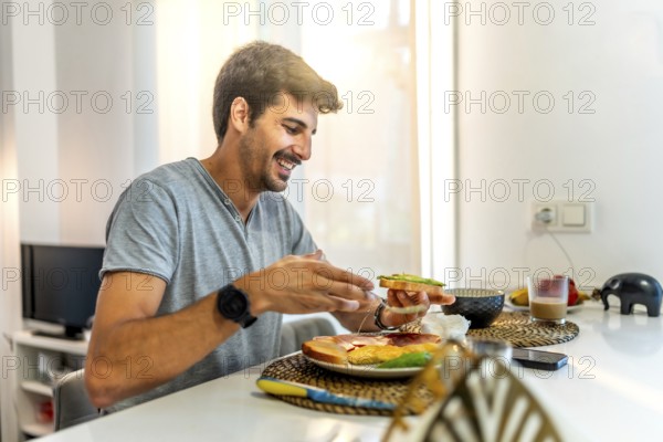 Young man smiling while enjoying a nutritious breakfast of avocado toast in a stylish, modern kitchen, embracing a healthy lifestyle