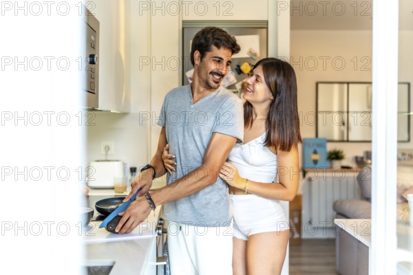 Romantic couple embracing while preparing a healthy breakfast together in a bright, modern kitchen, enjoying their morning routine
