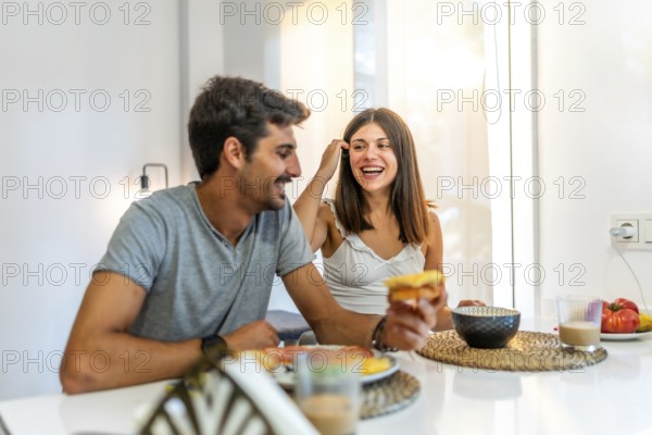 Young couple enjoying breakfast at home, laughing and sharing joyful moments together, creating a warm and loving atmosphere