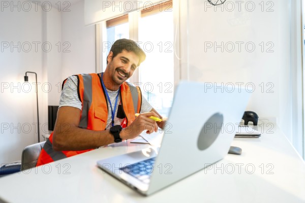 Young construction engineer wearing an orange safety vest working from home having a video conference on his laptop