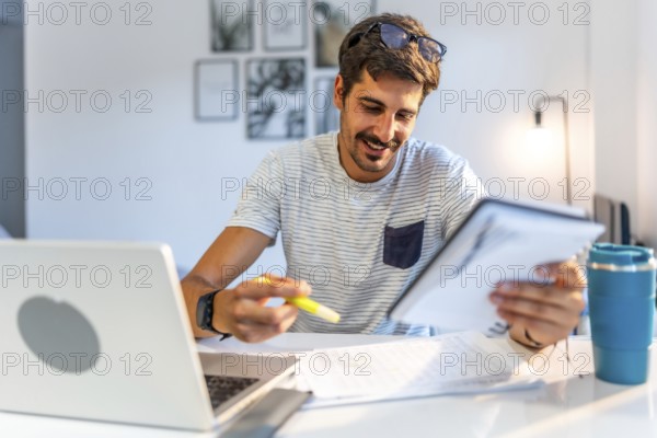 Young male freelancer comparing information on his tablet with data on his laptop, working from his modern home office