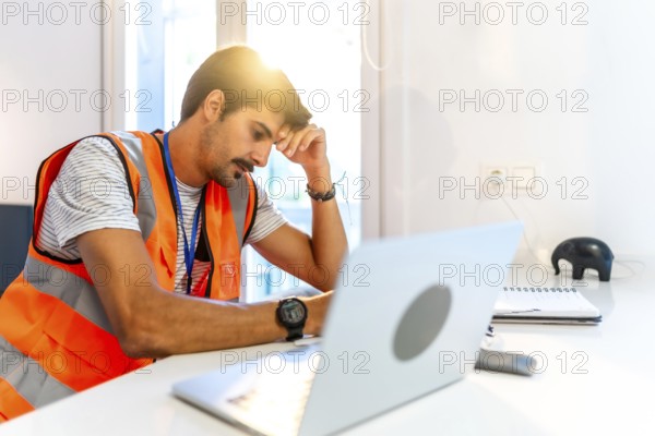 Young construction worker feeling stressed while working remotely from home using laptop, having problems and headache