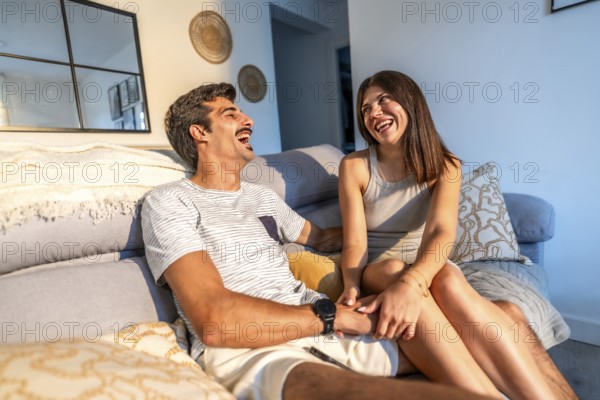 Young couple enjoying time together, laughing and holding hands while relaxing on a comfortable sofa in their modern living room