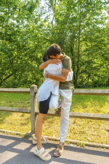 Romantic couple hugging near a wooden fence in a park, enjoying a sunny summer day surrounded by lush greenery