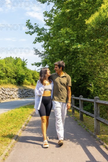 Young couple strolls along a paved path beside a road, enjoying each other's company on a sunny day
