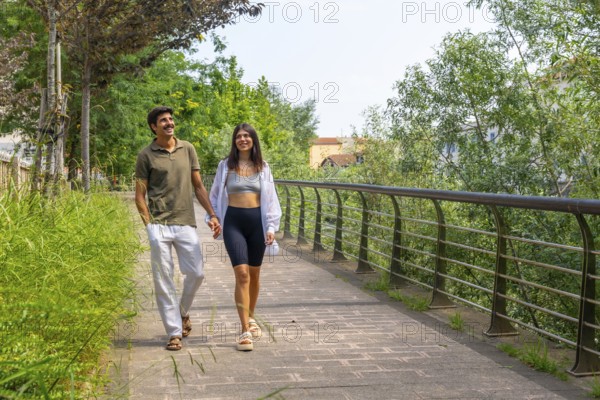 Happy couple enjoying a leisurely stroll, holding hands and walking along a paved path in a green city park