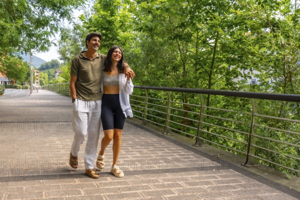 Young couple enjoying a leisurely stroll across a bridge in a green park, embracing the tranquility of nature