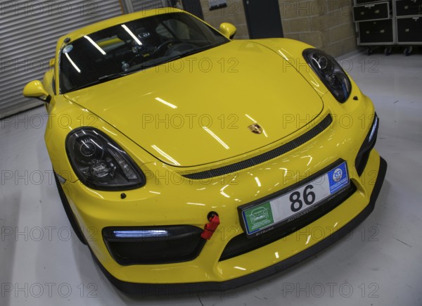 Dynamic photo front of sports car racing car yellow Porsche Cayman GT4 with front left mounted red tow strap, international
