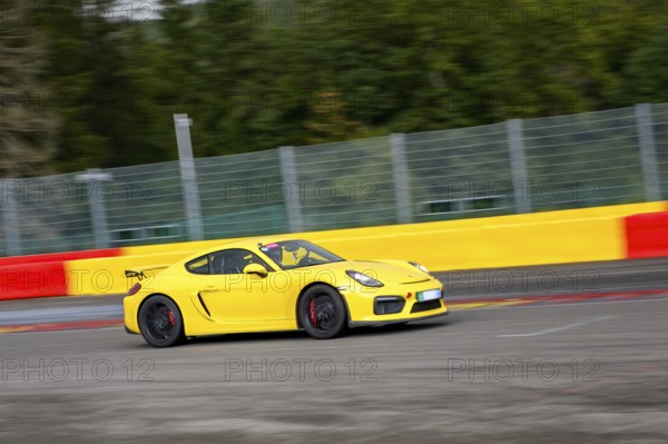 Yellow racing car sports car Porsche Cayman GT4 races at high speed top speed during trackday on FIA Formula 1 race track, Circuit de Spa Francorchamps, Ardennes rollercoaster, Ardennes, Malmedy, Belgium
