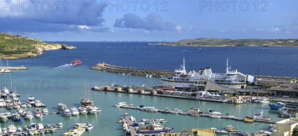 View of harbour basin of Gozo Mgarr Harbour with small boats yachts yachts, in the middle of the picture jetty for ferries from to Valletta island Malta and moored ferry car ferry, in the background part of Comino island, Mgarr, Gozo, Malta