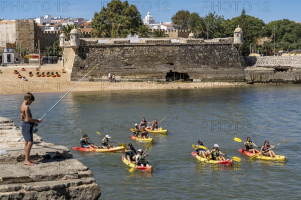 Kayak tours to the rocky coast Ponta da Piedade, groups of tourists in kayaks on the sea to the rugged coastal landscape, children fishing at the harbour, from Lagos, in the west of the Algarve, Portugal Forte Ponta da Bandeira