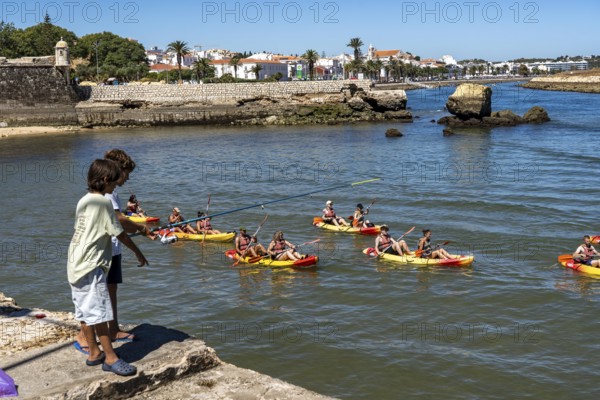 Kayak tours to the rocky coast of Ponta da Piedade, groups of tourists in kayaks on the sea to the rugged coastal landscape, children fishing at the harbour, from Lagos, in the west of the Algarve, Portugal